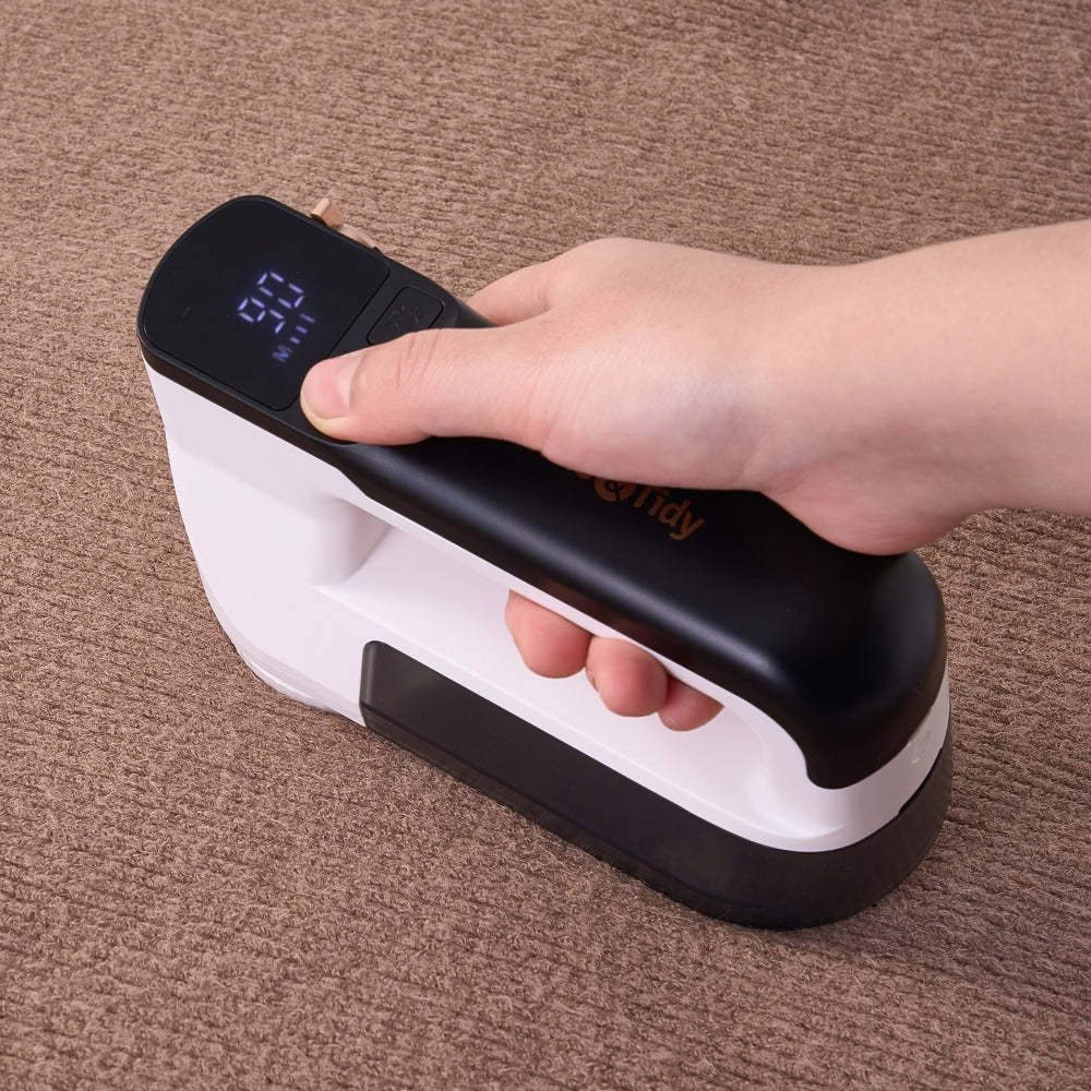 Hand holding a black and white fabric shaver on a brown couch showing LED display