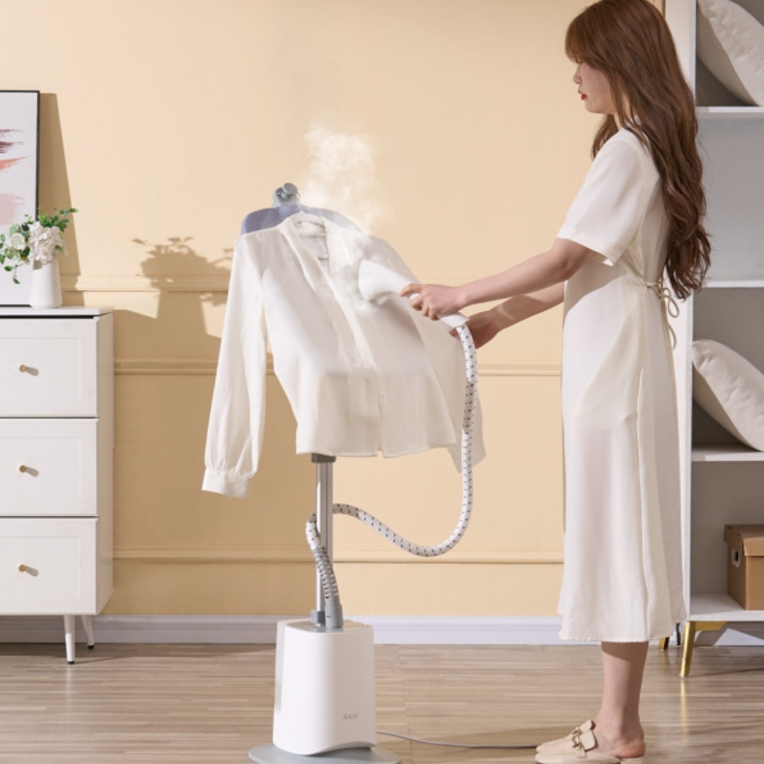 Woman ironing a white shirt on a standing ironing board in a room with a dresser and shelves.