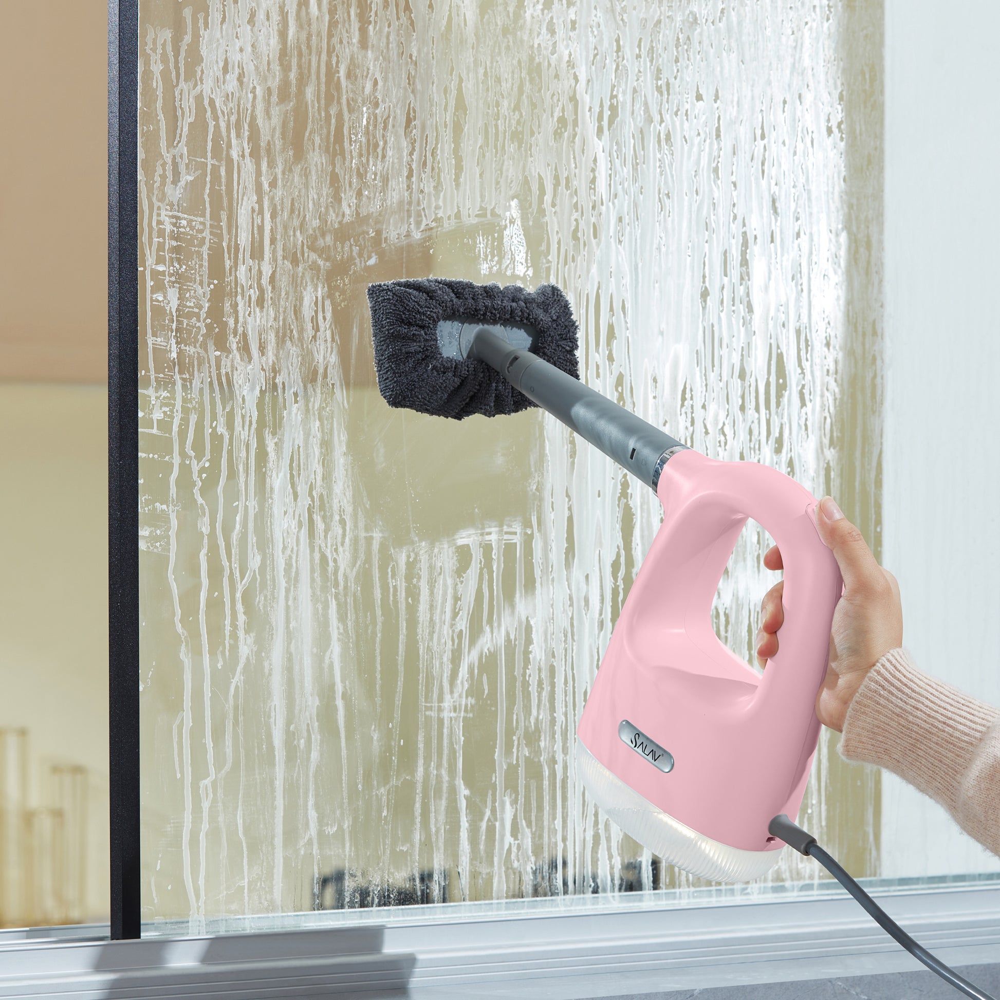 CS100PinkPerson cleaning a glass surface with a pink handheld steam cleaner.