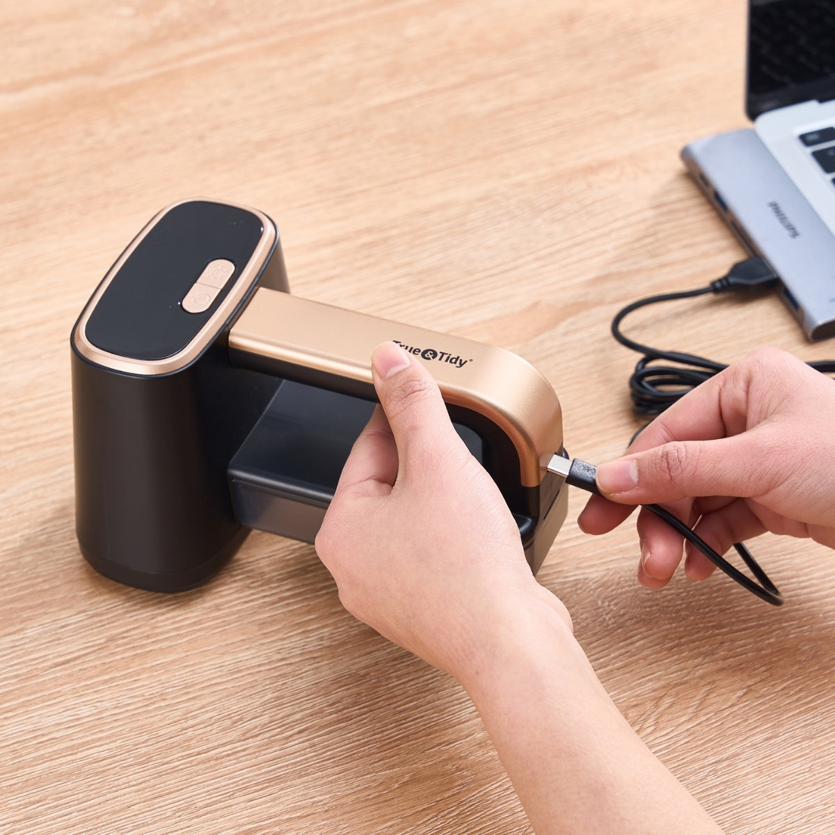 Person plugging a cable into a black and gold electronic device on a wooden surface