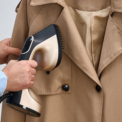 Person using a handheld steamer on a beige trench coat