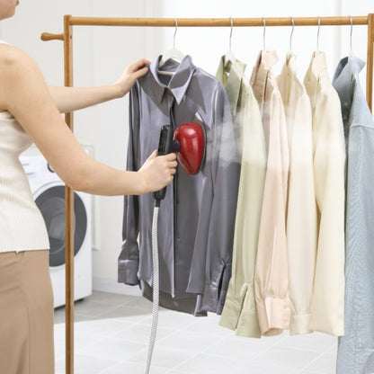 SS1500+Red+Person using a garment steamer on a shirt hanging on a rack with other shirts.