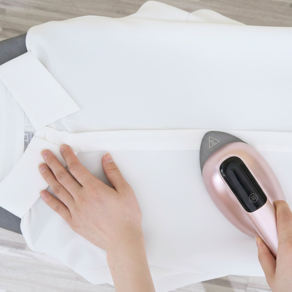 SS1500+RoseGold+Person using a handheld steamer to iron a white garment on an ironing board