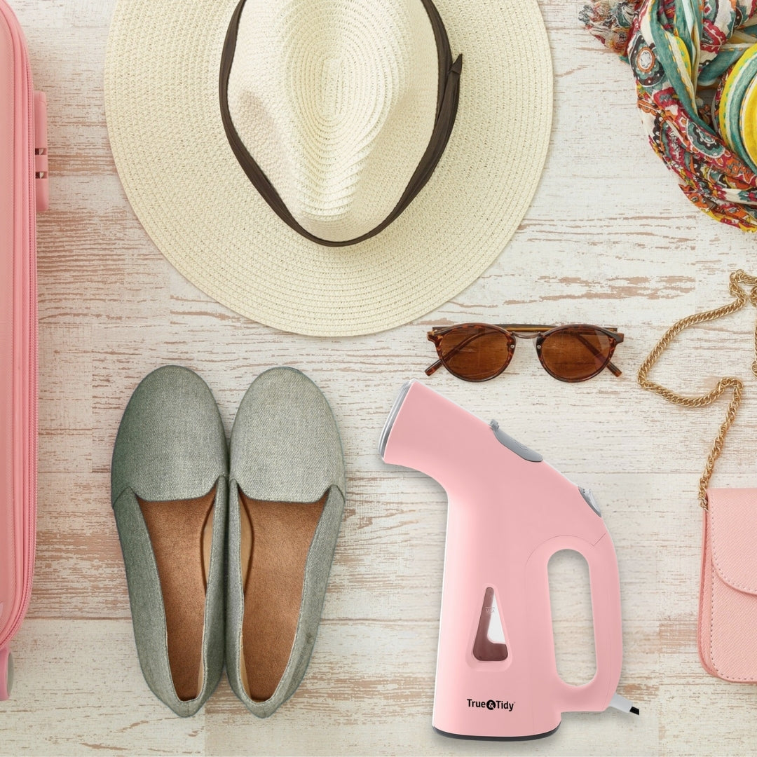 TS38 + Pink + Travel Essential + Gray loafers, white straw hat, pink handheld steamer, sunglasses, and pink pouch on a wooden surface.